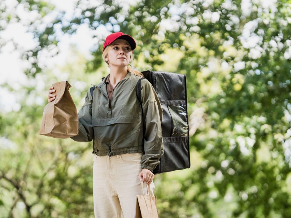 A StarOne driver standing outdoors with an insulated delivery bag and two orders.