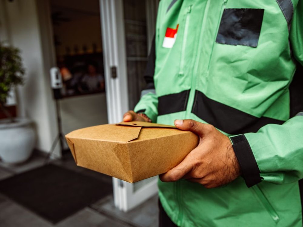 A delivery rider holding a sealed food package at a customer's door.